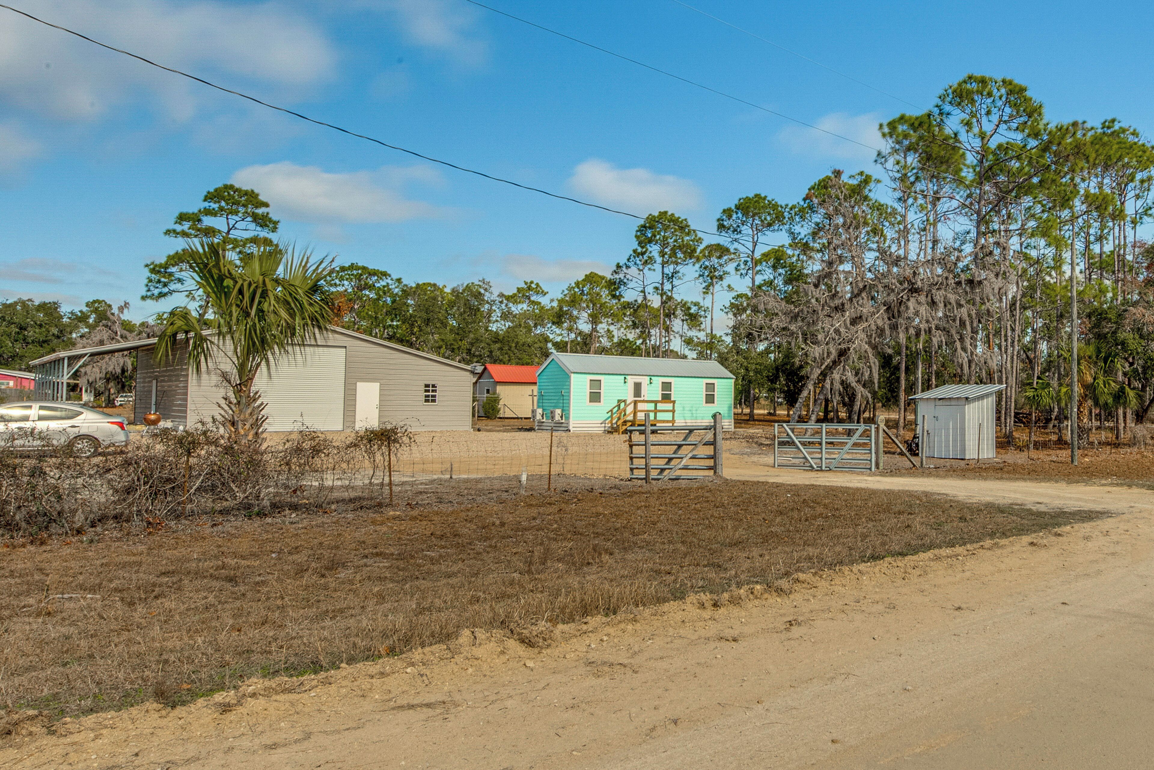 A rural property with a small house, a fenced yard, and a dirt road.