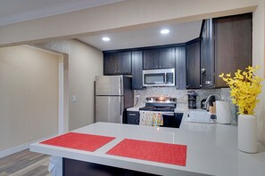 Una cocina moderna con armarios oscuros, electrodomésticos de acero inoxidable y encimera blanca.