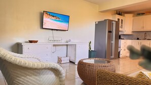 A modern living room with a flat-screen TV, white furniture, and a kitchen area. - Near Rodney Bay! Breezy, Beachy and Spacious 1-Bedroom Unit. (Castries)