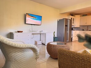 A modern living room with a flat-screen TV, white furniture, and a kitchen area. - Near Rodney Bay! Breezy, Beachy and Spacious 1-Bedroom Unit. (Castries)