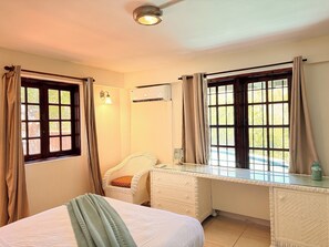 A bedroom with a bed, a desk, a chair, and two windows with curtains. - Near Rodney Bay! Breezy, Beachy and Spacious 1-Bedroom Unit. (Castries)