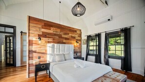 Ein Schlafzimmer mit Holz-Kopfteil, einem großen Bett, einer Bank am Fußende und Blick ins Freie durch das Fenster.