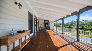 Una terraza de madera con barandilla, una mesa con un jarrón y vistas a la vegetación.
