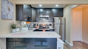 A modern kitchen with dark cabinets, stainless steel appliances, and a central island with bar stools. - Sip, Golf & Explore: Pleasanton Retreat! (Pleasanton)