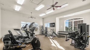 A gym with various exercise equipment, large windows, and ceiling fans.