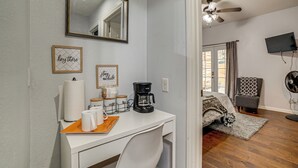 A hotel room with a white desk, a coffee maker, a mirror, and a bed with a patterned bedspread. - Sip, Hike & Explore: Quiet SoCal Studio w/ Patio! (Winchester)