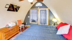 A bedroom with a sloped ceiling, a bed with blue bedding, a wooden dresser, a chair, and a window with curtains. - 1 Mi to TIEC: Peaceful Mountain Cabin (Mill Spring)
