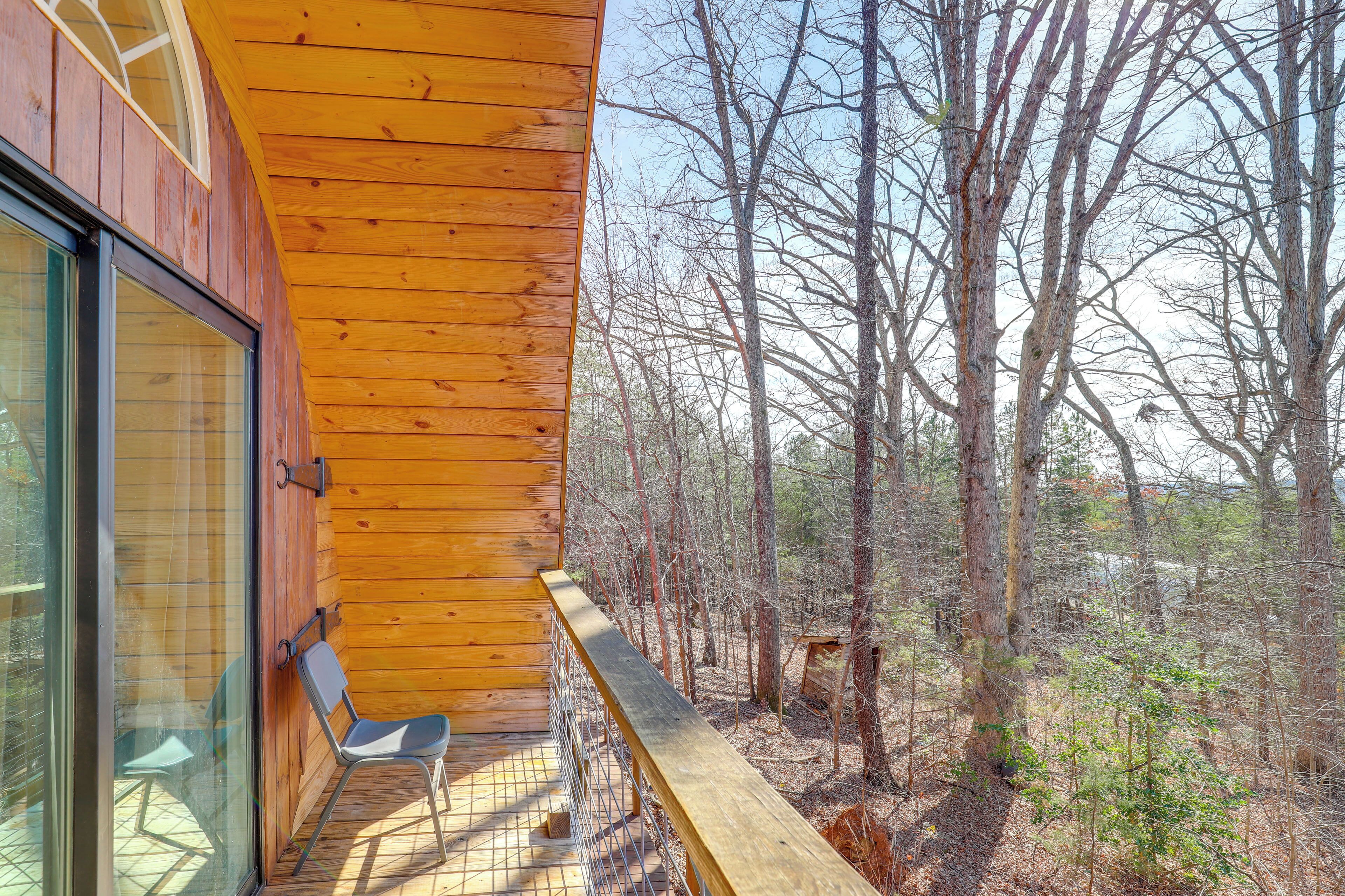 A wooden balcony with a metal railing overlooking a forested area.