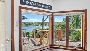 Ett rum med ett stort fönster märkt med texten ”VINEYARD HAVEN”, med utsikt över en terrass och en sjö samt träd.