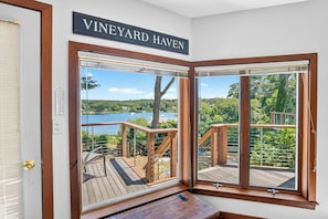 Ein Zimmer mit einem großen Fenster mit der Aufschrift 'VINEYARD HAVEN' und Blick auf eine Terrasse, von der aus man einen See und Bäume sieht.