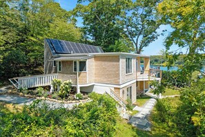 A two-story house with a solar panel roof, a deck, and a view of a lake. - Steps to Beach: Martha's Vineyard Private Retreat! (Vineyard Haven)