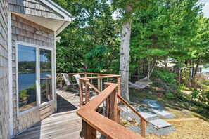 A wooden deck with a view of a lake, outdoor furniture, and a hammock. - Steps to Beach: Martha's Vineyard Private Retreat! (Vineyard Haven)