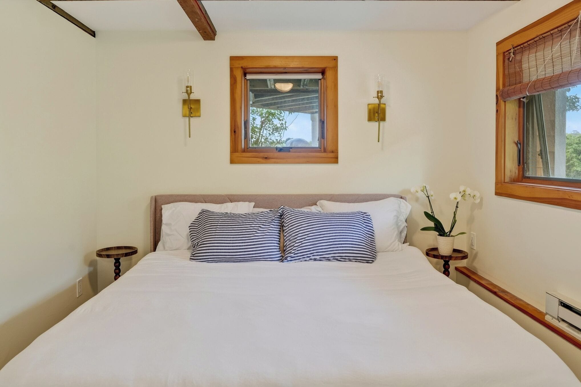 A neatly made bed with two pillows, a small bedside table with a lamp, and a window with a view of trees.