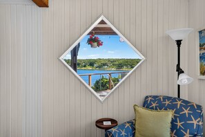 A room with a view of a lake through a diamond-shaped mirror, a lamp, and a patterned sofa. - Steps to Beach: Martha's Vineyard Private Retreat! (Vineyard Haven)