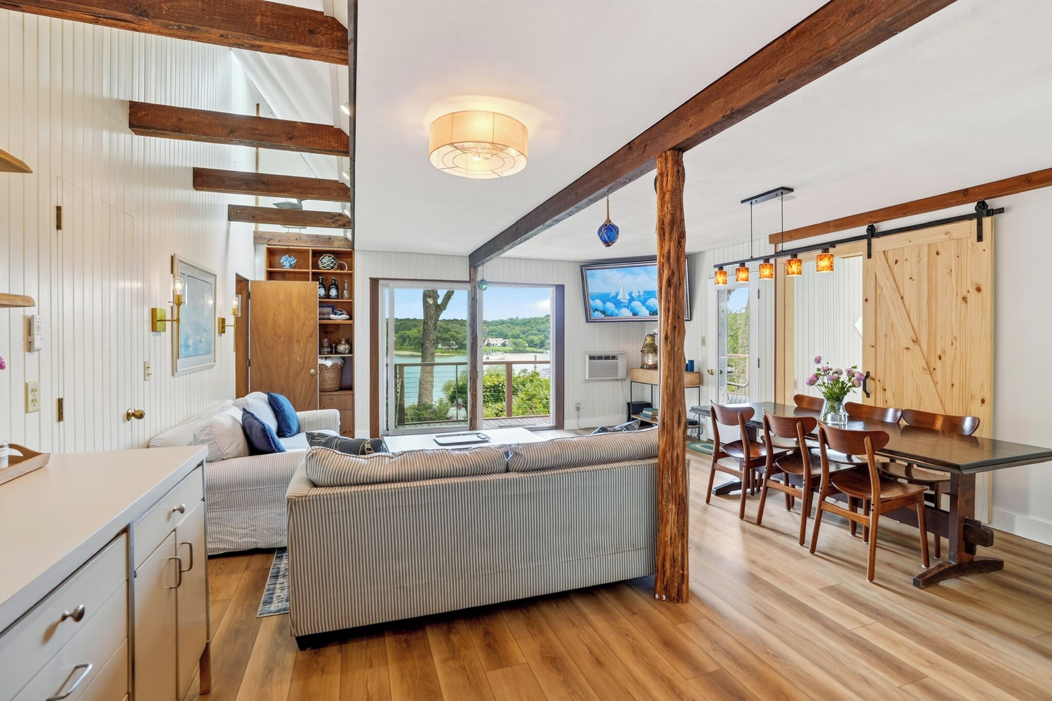 A modern interior with a wooden dining table, a sofa, and a kitchen area with a view to the outdoors.