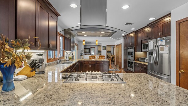 Una cocina moderna con armarios de madera oscura, encimeras de granito y electrodomésticos de acero inoxidable, con una isla central.