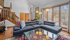 Una sala de estar moderna con un sofá modular, una mesa de centro de vidrio y una escalera con barandilla de madera.