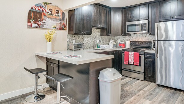 A modern kitchen with dark wood cabinets, stainless steel appliances, a granite countertop, and a bar stool. - Shop, Hike & Sip Wine: Pleasanton Gem w/ Balcony! (Pleasanton)