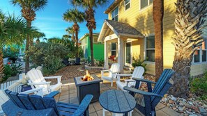 A patio with Adirondack chairs, a fire pit, and a house with a green door. - Sweet & Salty by Avantstay Walk to Beach + Community Pool + Firepit (Port Aransas)