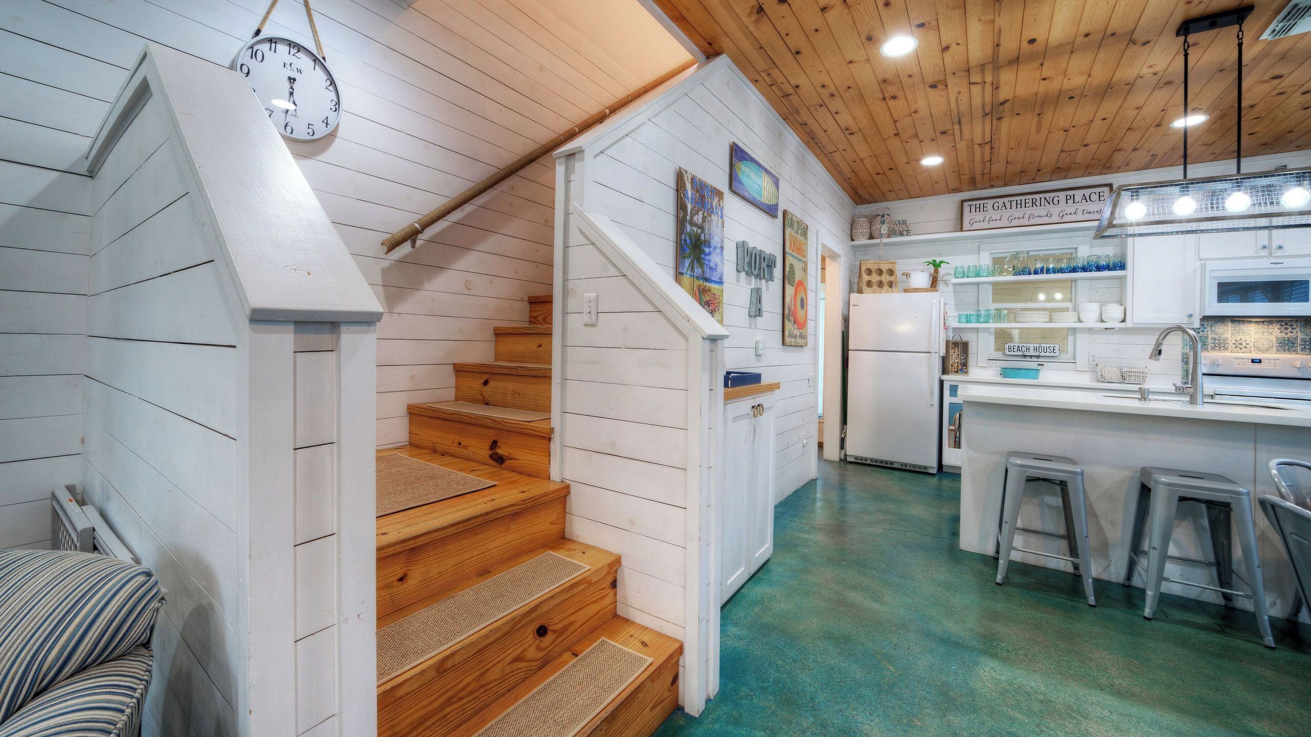 Una cocina con escaleras de madera, un reloj y un cartel que dice 'The Gathering Place'.