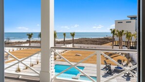A balcony with a view of the beach, a pool, and outdoor furniture. - Paradise at the Pointe (Ocean Isle Beach)