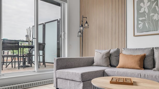 A modern living room with a grey sofa, a round coffee table, and a view through a glass door to an outdoor patio. - Magnificent downtown Penthouse with free underground parking (Québec)