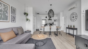 A modern living room with a grey sofa, a coffee table, and a dining area with a wooden table and chairs. - Magnificent downtown Penthouse with free underground parking (Québec)