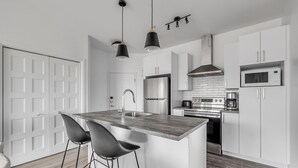 A modern kitchen with a central island, stainless steel appliances, and a white color scheme. - Magnificent downtown Penthouse with free underground parking (Québec)