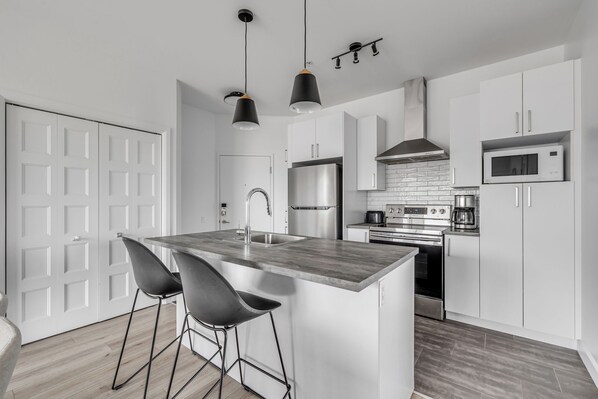 A modern kitchen with a central island, stainless steel appliances, and a white color scheme. - Magnificent downtown Penthouse with free underground parking (Québec)