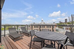 A rooftop terrace with a round table and four lounge chairs, overlooking a cityscape with historic buildings and a clear sky. - Magnificent downtown Penthouse with free underground parking (Québec)