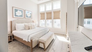 Ein Schlafzimmer mit einem Bett, Nachttischen, einem Deckenventilator, großen Fenstern mit Jalousien, einem Fernseher und einer Marmorplatte.