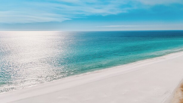 Ein Strand mit klarem türkisblauem Wasser und einem weiten Sandufer.