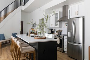Een moderne keuken met een centraal eiland, roestvrijstalen apparatuur en een houten trap.