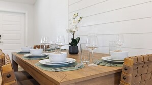 Una mesa de comedor dispuesta con cuencos, platos y cubiertos blancos, flanqueada por sillas con respaldo trenzado.