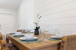 A dining table set with white bowls, plates, and cutlery, flanked by chairs with woven backs. - Poolside Paradise with Brand New Spa & Saltwater Pool – Minutes to Siesta Key (Sarasota)