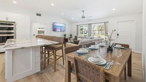 Una cocina moderna con una isla de mármol, una mesa de comedor de madera para cuatro personas y un horno empotrado.