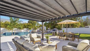 Un patio cubierto con mobiliario de mimbre, una piscina y una parrilla.