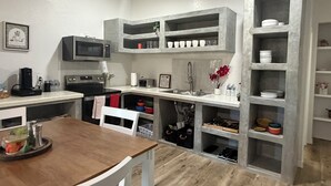 Eine kleine Küche mit integrierten Geräten, ein Essbereich mit einem Holztisch und Regale zur Aufbewahrung.