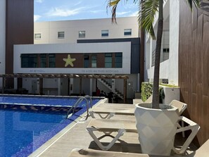Una piscina con sillas de descanso y un edificio con un logotipo de estrella y texto.