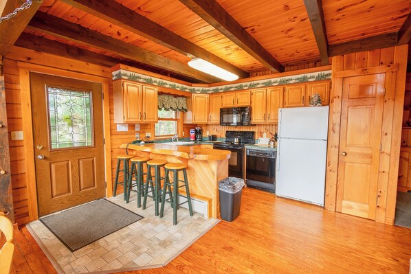 A wooden cabin kitchen with a bar area, wooden cabinets, a refrigerator, and a microwave.