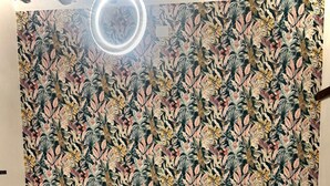 Ein Schlafzimmer mit einem großen Bett, einem gepolsterten Kopfteil, zwei Nachttischen mit Lampen und einer Wand mit tropischem Blattmuster.