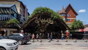 A building with a sign reading "Natal Luz" and a covered entrance area with potted plants. - Apto com Vaga Aquecimento e Piscina na Vila Su a (Gramado)