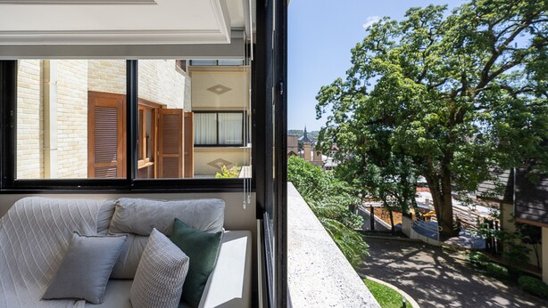 Une pièce avec un canapé et des coussins, une fenêtre donnant sur un arbre et des immeubles.