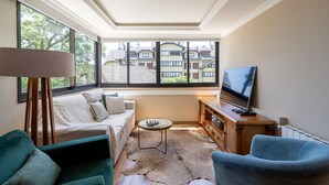 Un salon chaleureux avec un canapé, un fauteuil bleu, une petite table ronde et un téléviseur posé sur un meuble en bois.