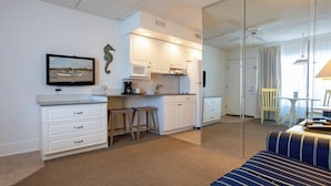 A modern kitchen with white cabinets, a microwave, and a coffee maker. There is a sofa with striped cushions in the living area.