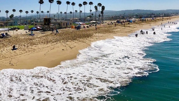 A beach with palm trees, a lifeguard tower, and people on the sand.