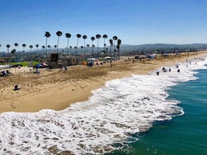 A beach with palm trees, a lifeguard tower, and people on the sand. - Cozy 3BR/2BA Beachside Escape in Huntington Beach - Your Perfect Getaway Awaits! (Huntington Beach)