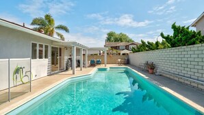 A swimming pool with a white fence and a covered patio area.