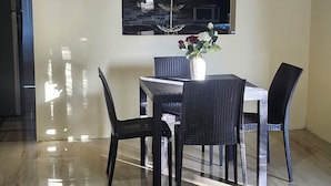 A dining area with a table and chairs, a vase with flowers, and a kitchen in the background.