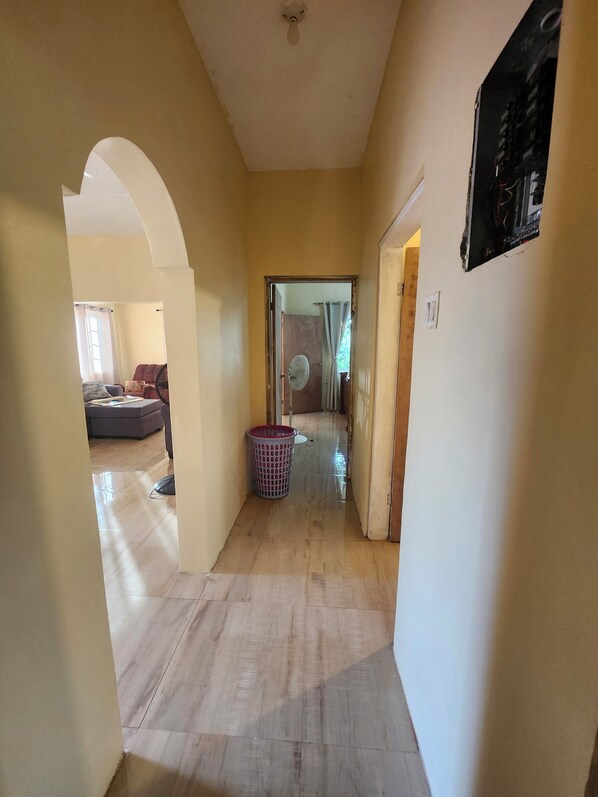 A hallway with a wooden floor, a laundry basket, and a ceiling fan. - Private home away from home south coast St Elizabeth (Jamaica)